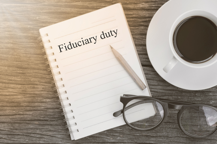 Concept Fiduciary duty message on notebook with glasses, pencil and coffee cup on wooden table.
